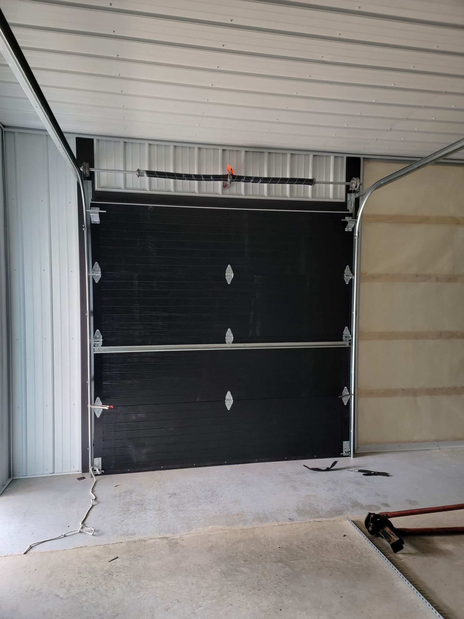 Partially installed black garage door inside a framed garage opening