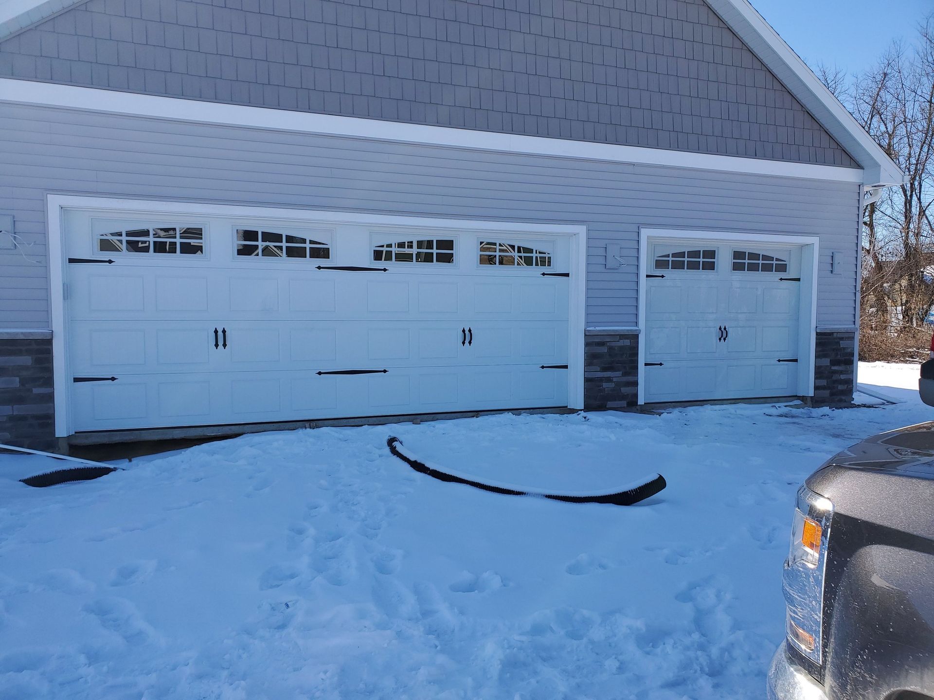 Snow-covered house with three white garage doors and part of a car at the right edge