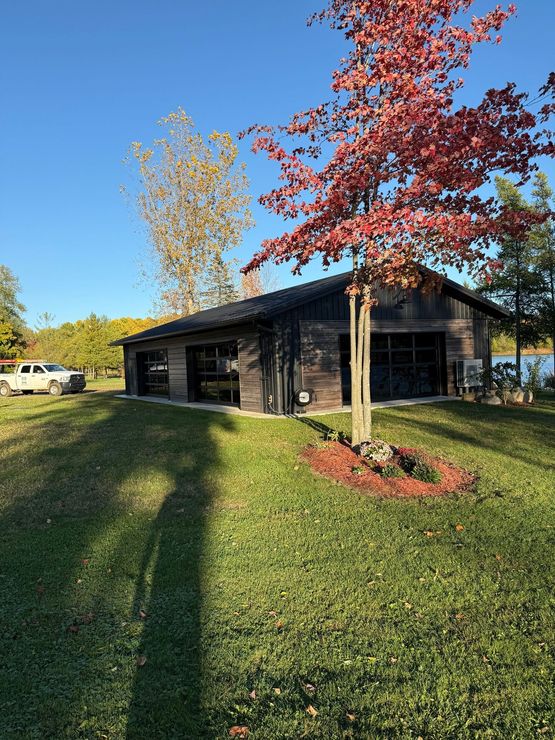 Black wooden building beside a grassy lawn with red and yellow trees on a sunny day