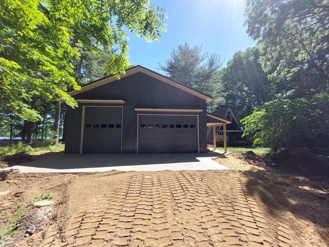 Brown garage with two doors at the end of a brick driveway, surrounded by trees in bright daylight