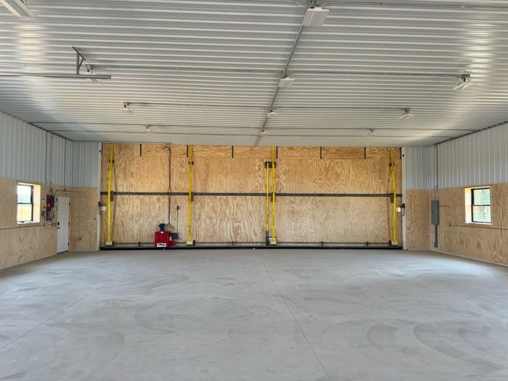 Empty metal warehouse interior with unfinished walls, concrete floor, and a red tool near the back wall