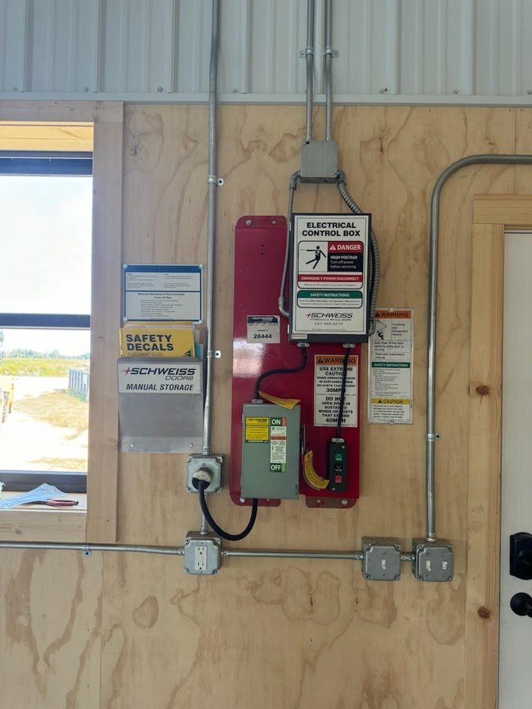 Wall-mounted fire alarm equipment and electrical boxes on plywood in a utility room.