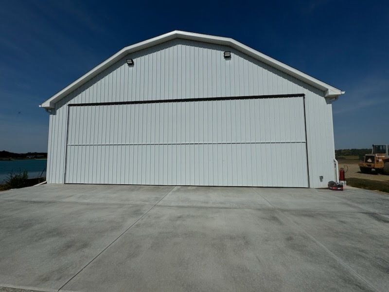 Large white hangar-style building with a concrete apron under a clear blue sky