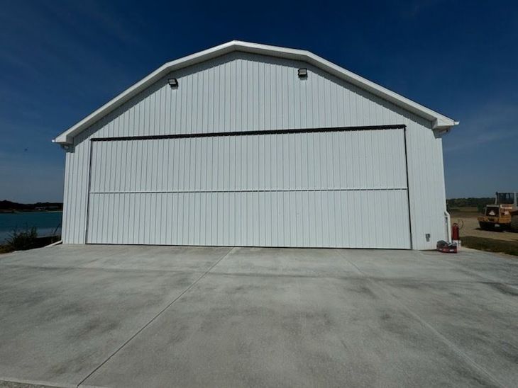 Large white metal hangar with closed doors on a concrete lot under a clear blue sky