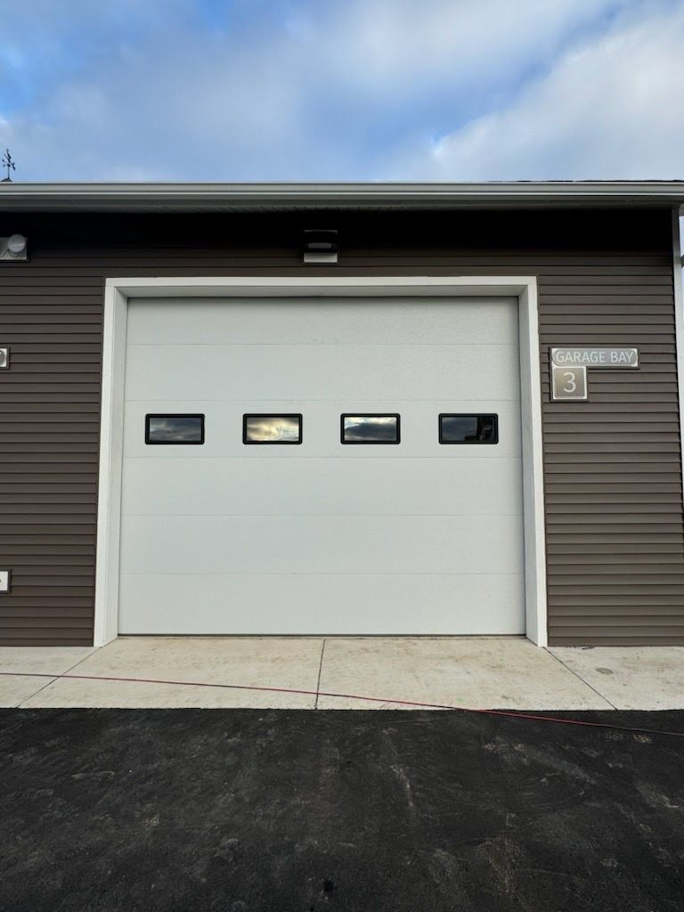 White garage door with four small windows on a modern dark-sided building