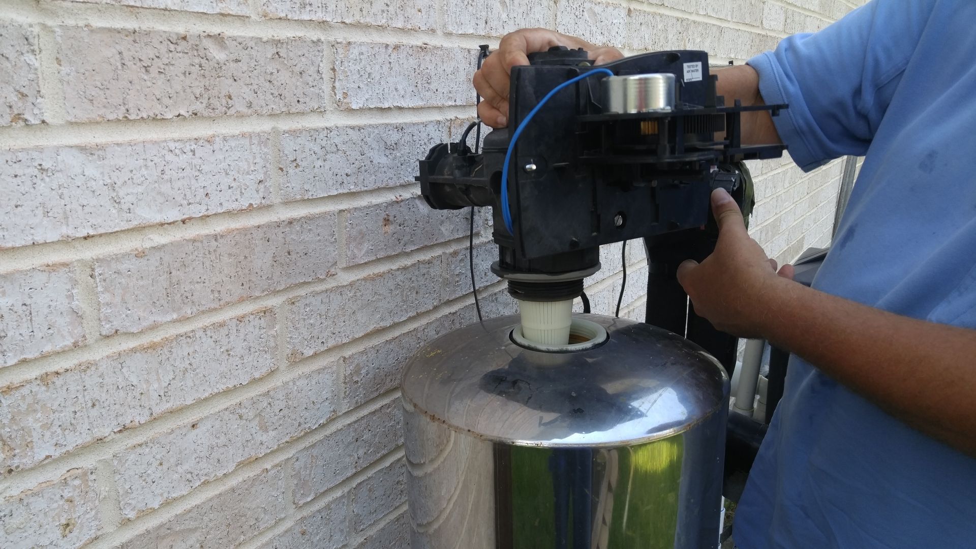 Technician removing the control valve from a water softener tank during a repair in Tomball, Texas.