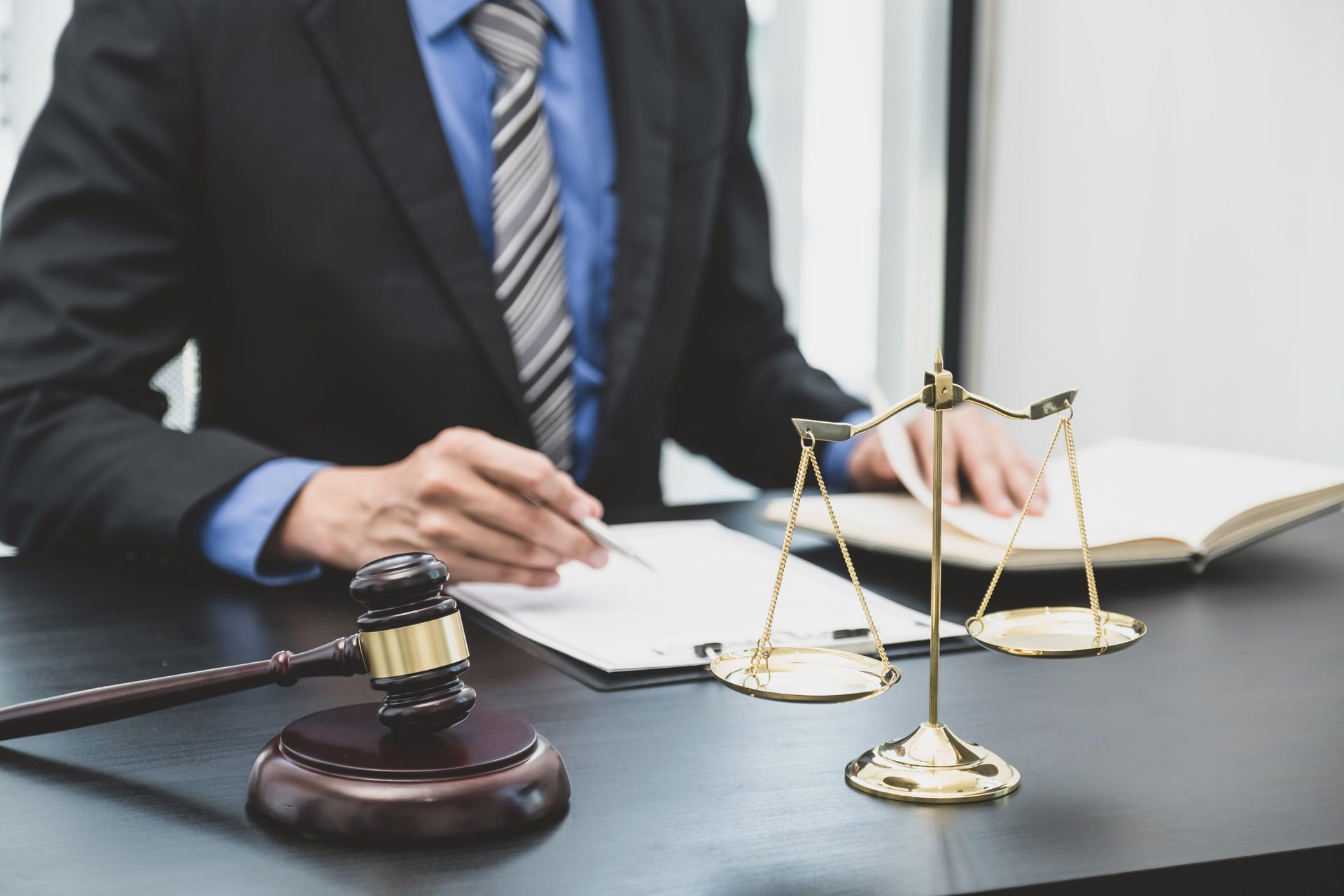 A professional in a suit and tie sits at a desk with a gavel and a scale of justice, writing on a document.
