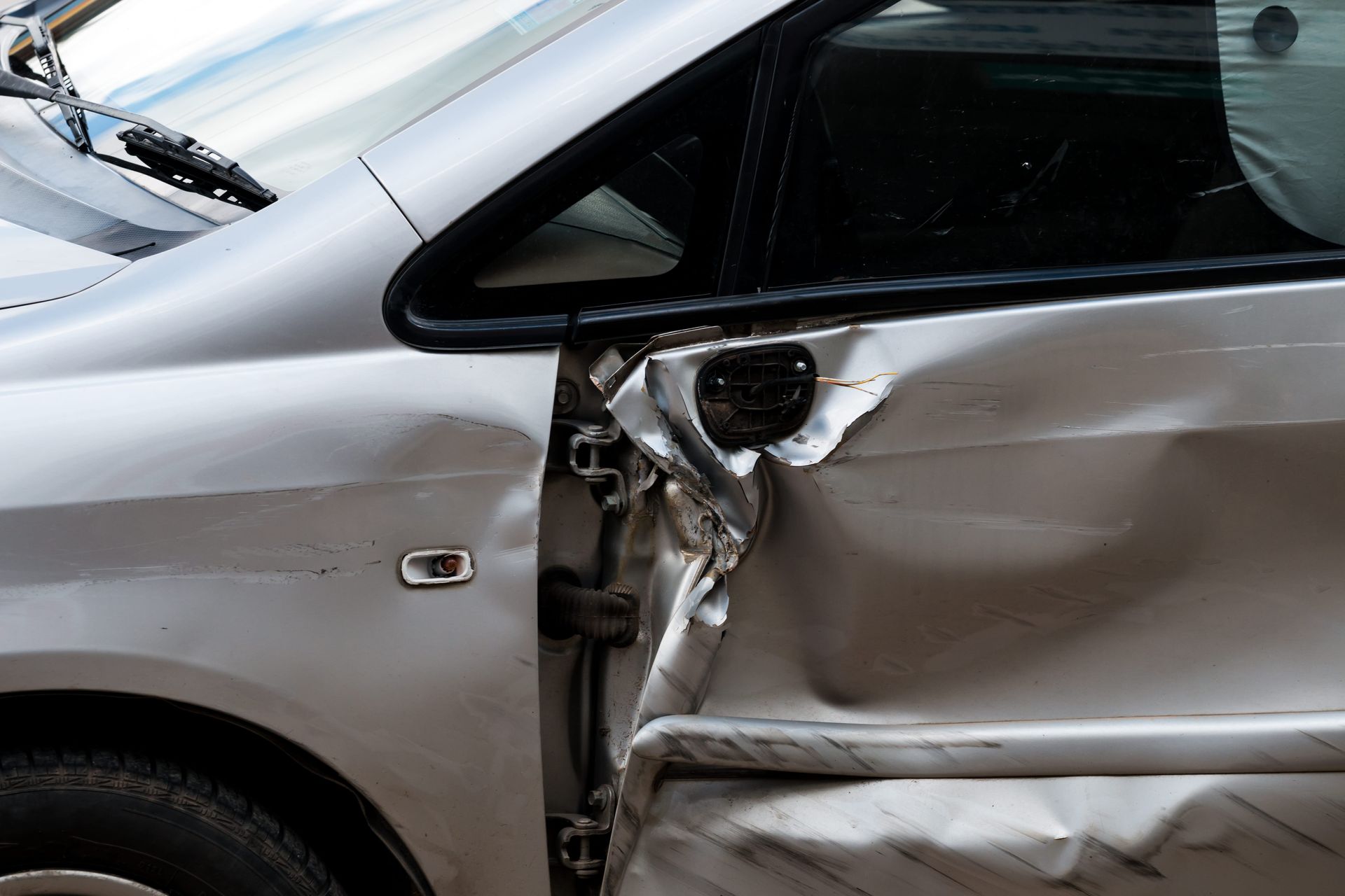Silver car with severe side damage and a crumpled door after a collision