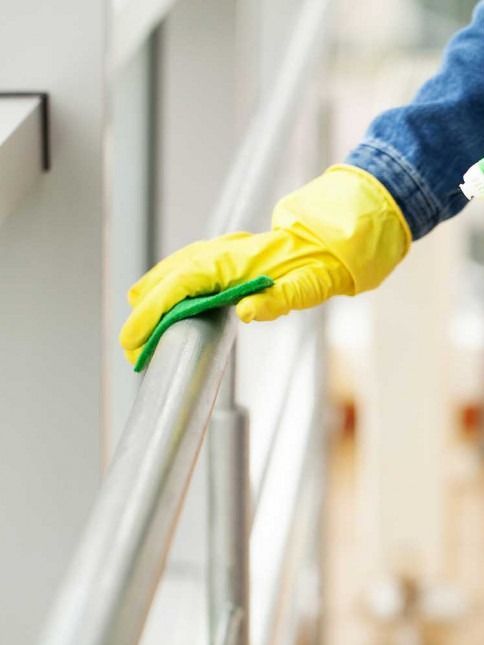 Hand in yellow glove wiping a metal railing.