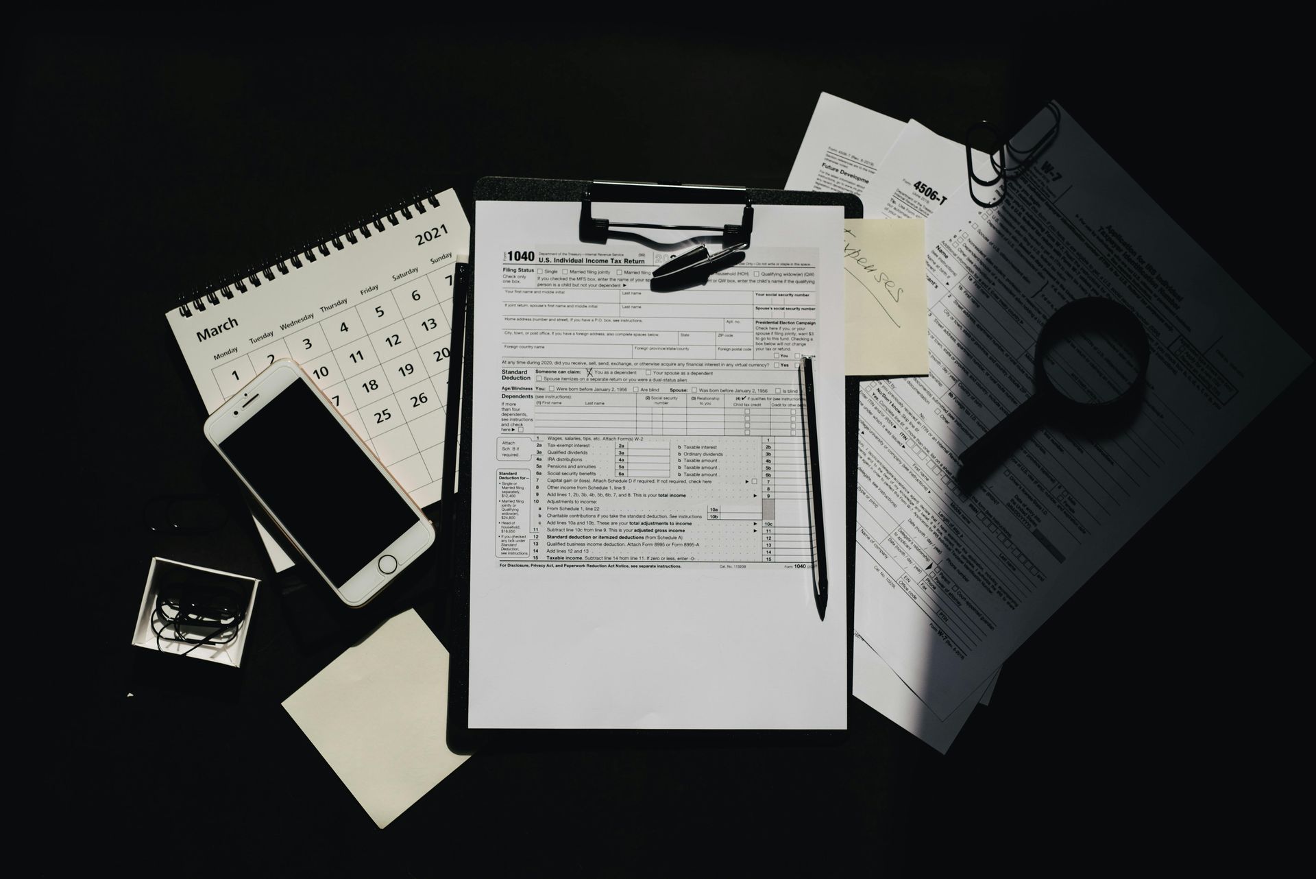 Desk with papers, calendar, phone, magnifying glass, and pencil in natural light.