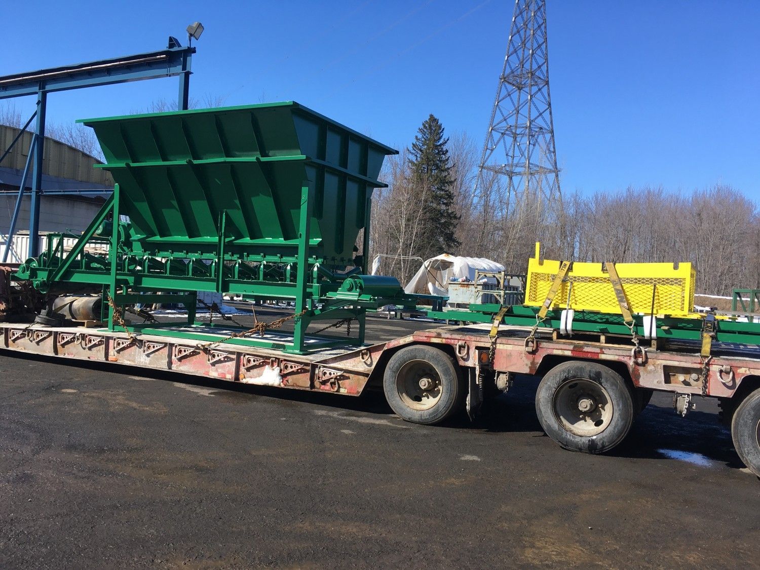 Machines vertes sur un camion à plateau, probablement à usage agricole, contre un ciel bleu.