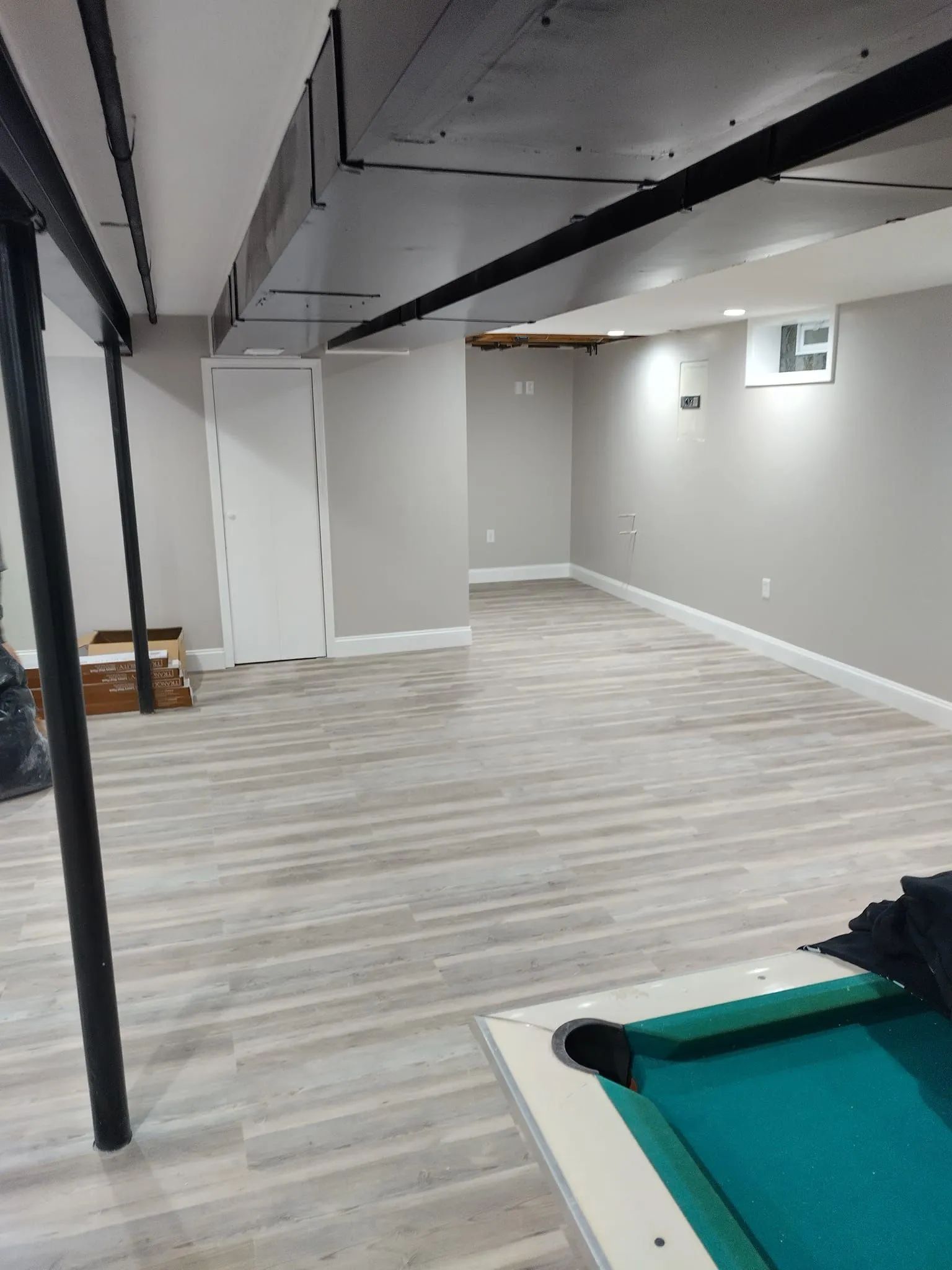 Finished basement with light wood-look flooring, neutral walls, and a pool table.