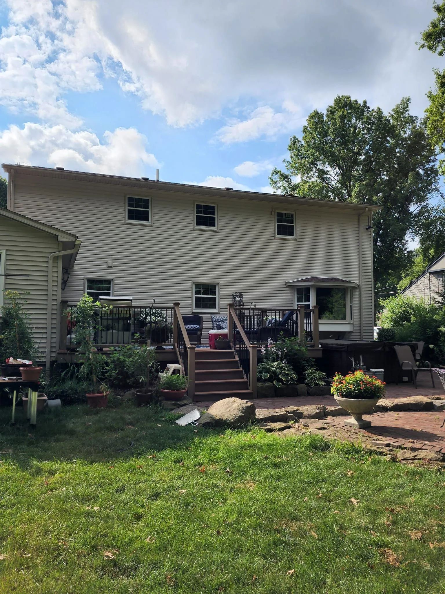 Backyard with a white two-story house, wooden deck, and green lawn under a partly cloudy sky