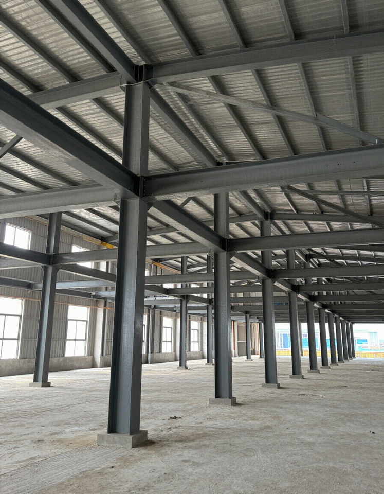 Empty industrial warehouse interior with steel columns and metal roof framework over a concrete floor