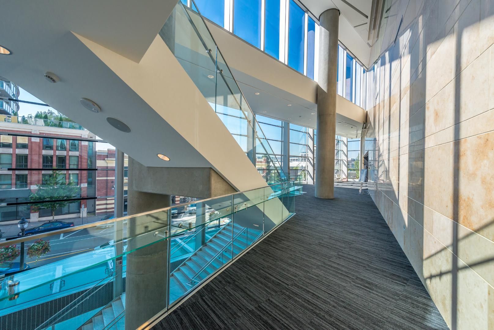 Interior view of a modern building with a glass-walled walkway overlooking an outdoor area.