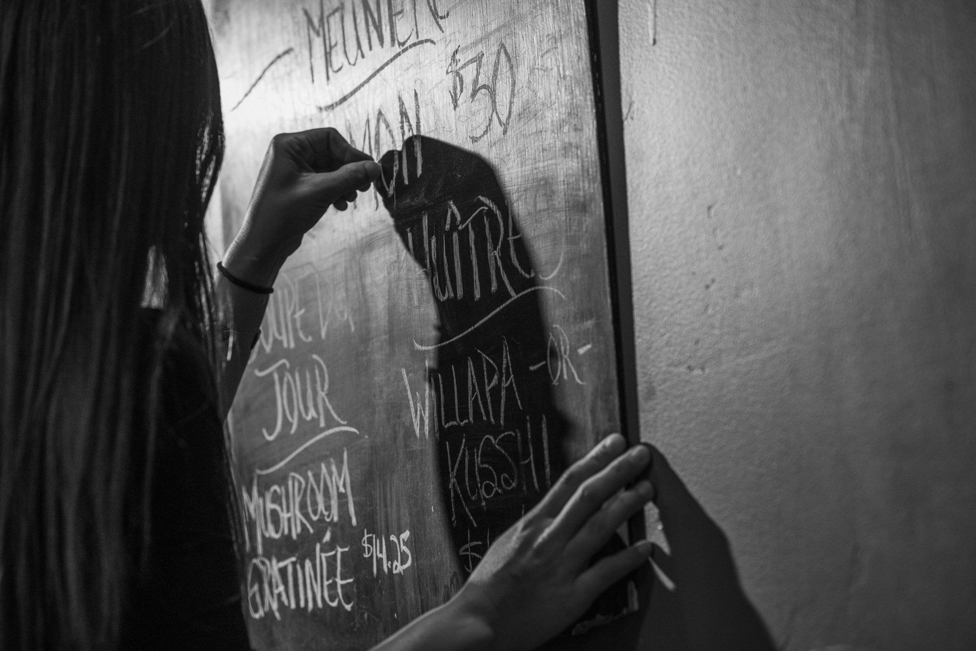 A woman is writing on a blackboard with chalk.