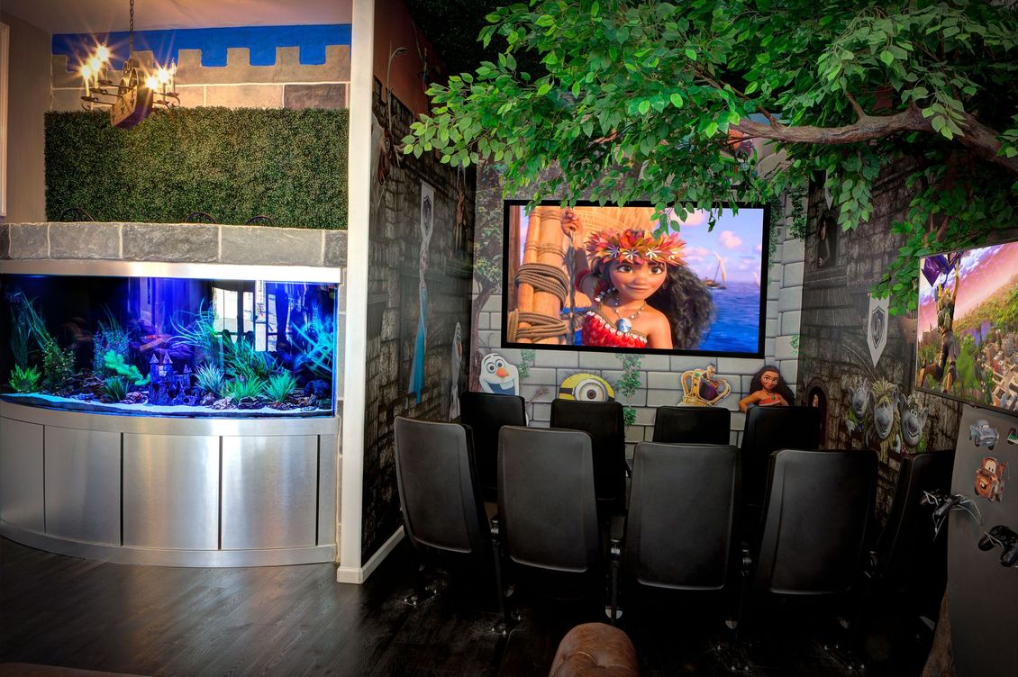 Outdoor patio with a large TV, black chairs, and a lit aquarium beside a leafy wall