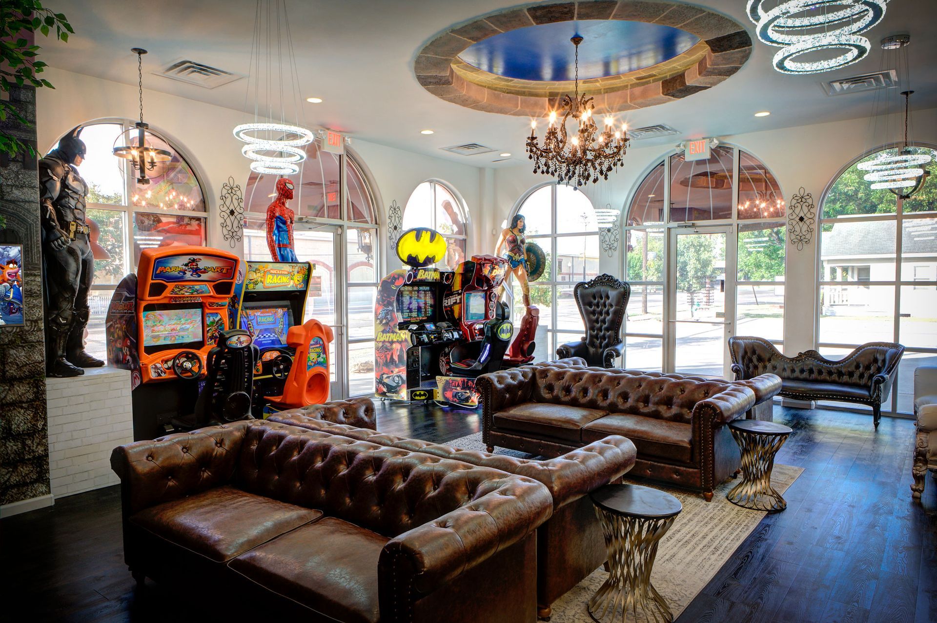 Upscale lounge with brown leather sofas, arcade machines, chandeliers, and arched windows.