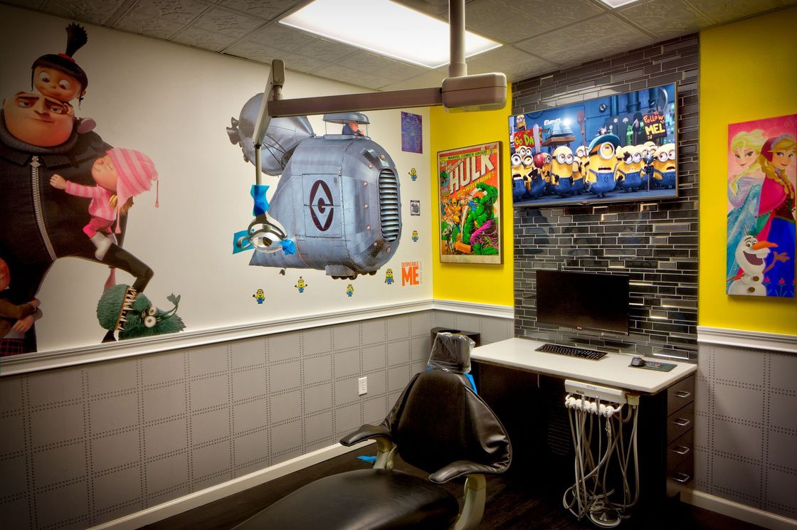 Colorful gaming room with computer desk, monitor, black chair, and cartoon wall art.