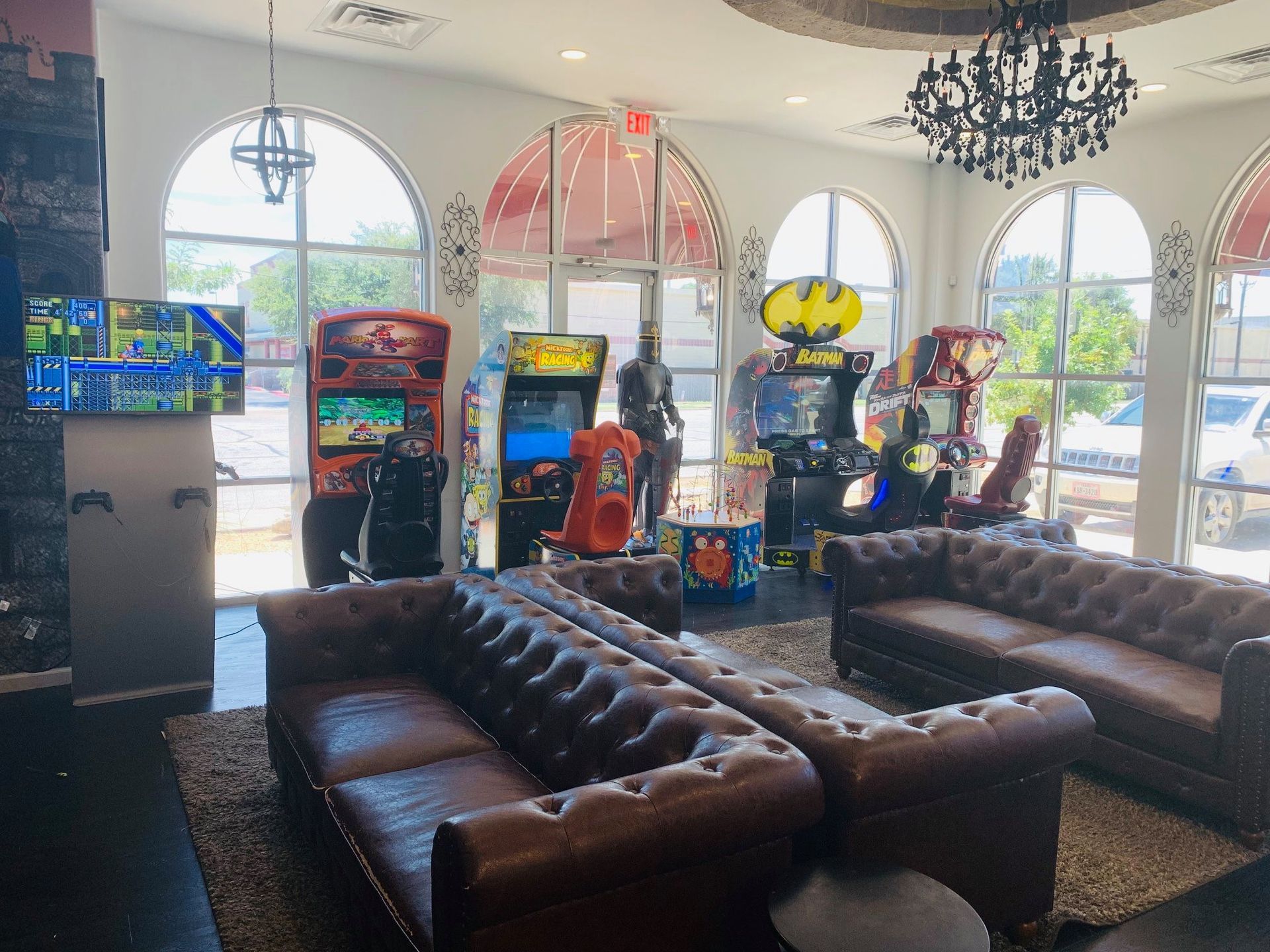 Arcade lounge with leather sofas, arcade machines, and large arched windows overlooking a bright exterior