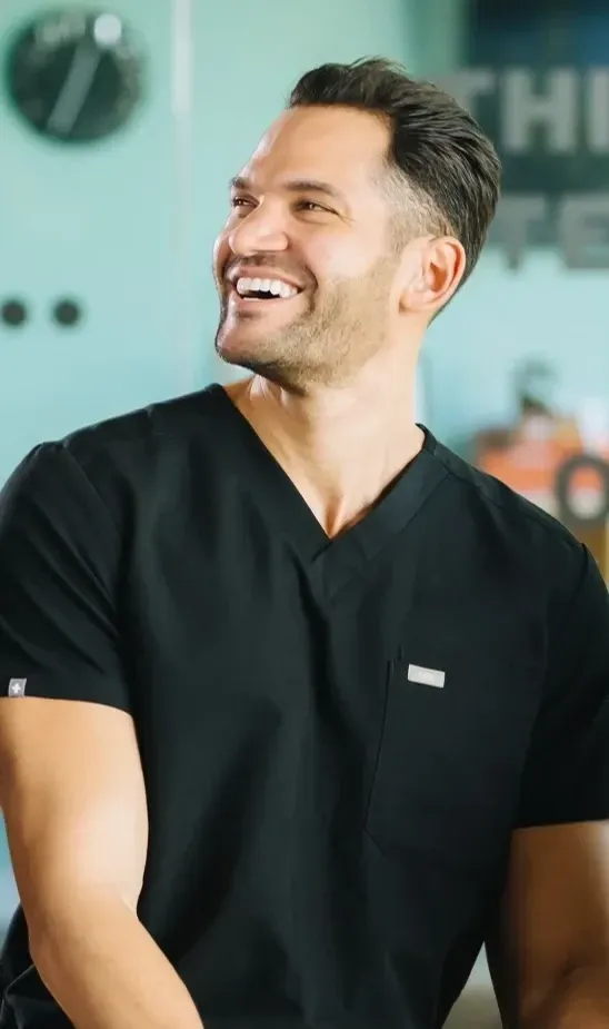 Smiling man in a black shirt standing indoors against a teal background