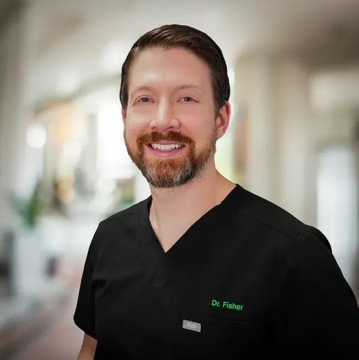 Smiling medical professional in black scrubs with green name embroidery in a bright hallway