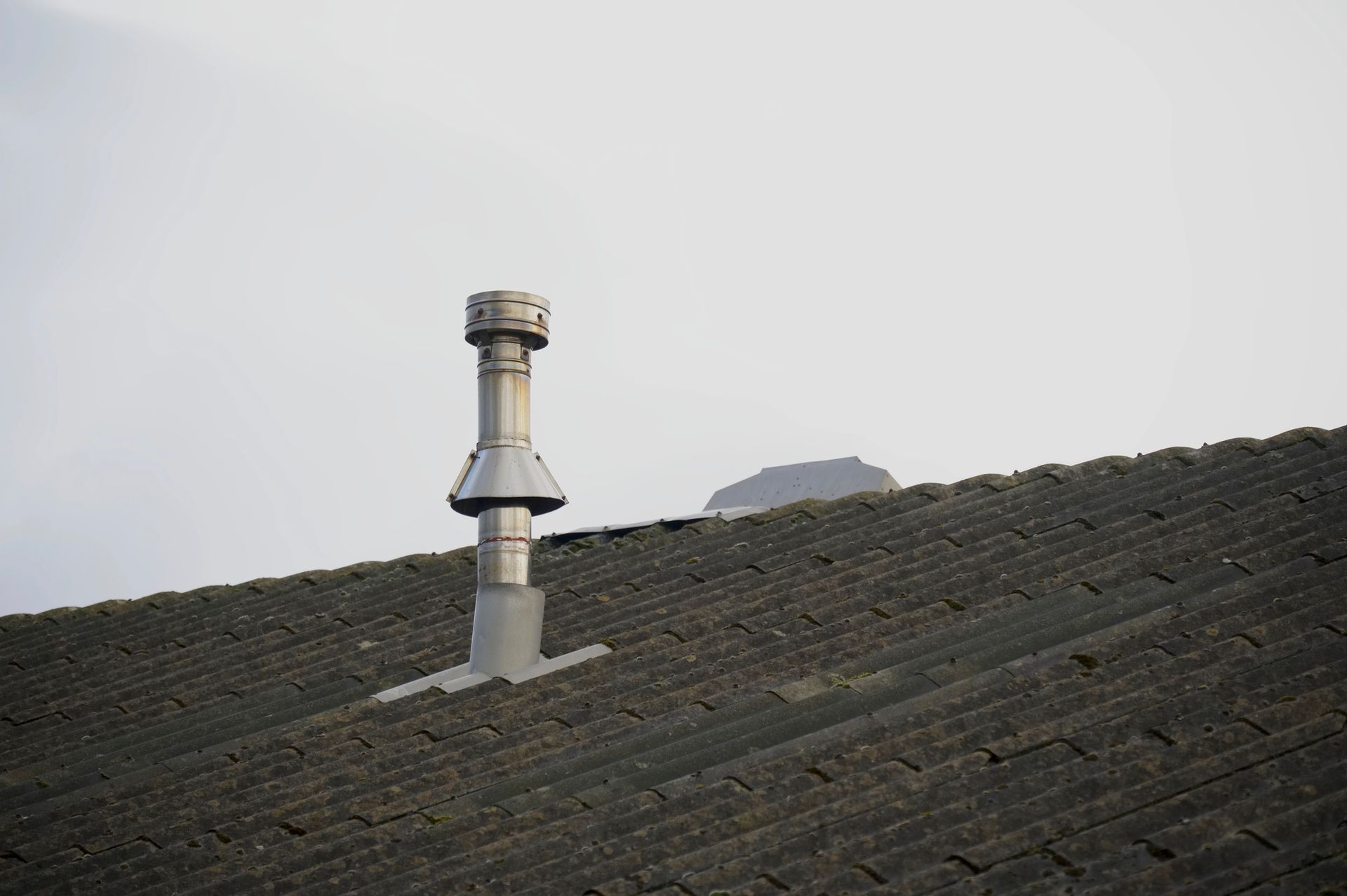 Tubo di ventilazione sul tetto con tappo su un tetto di tegole scure sotto un cielo grigio