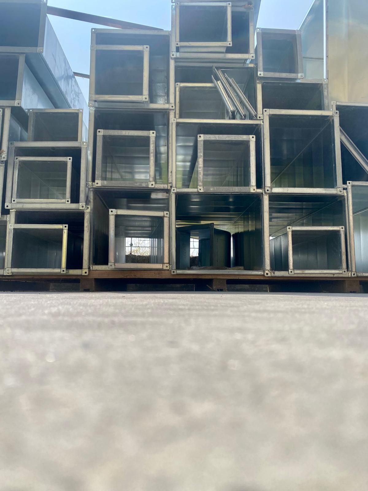 Condotti metallici quadrati impilati in un'area industriale sotto un cielo azzurro