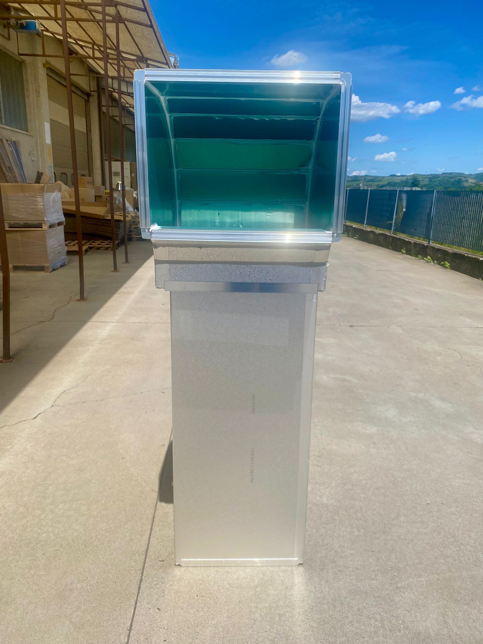 Podio in acrilico trasparente su una terrazza panoramica, illuminato dal sole, con l'oceano e il cielo azzurro sullo sfondo.