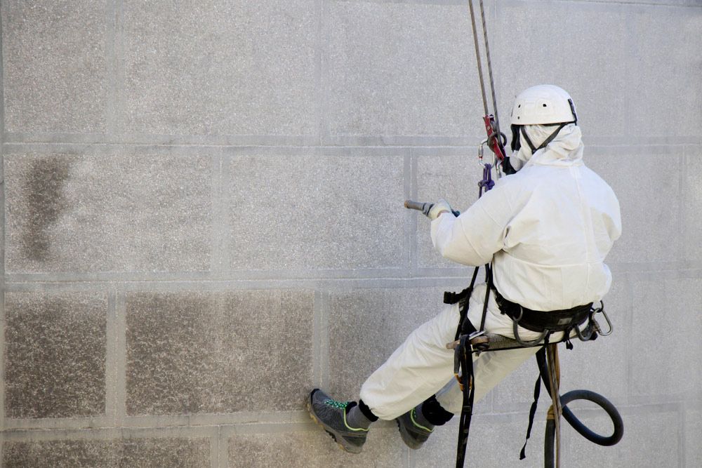 A Man in A White Suit Is Cleaning a Wall with A Hose — Haydyn's Cleaning In Craignish, QLD