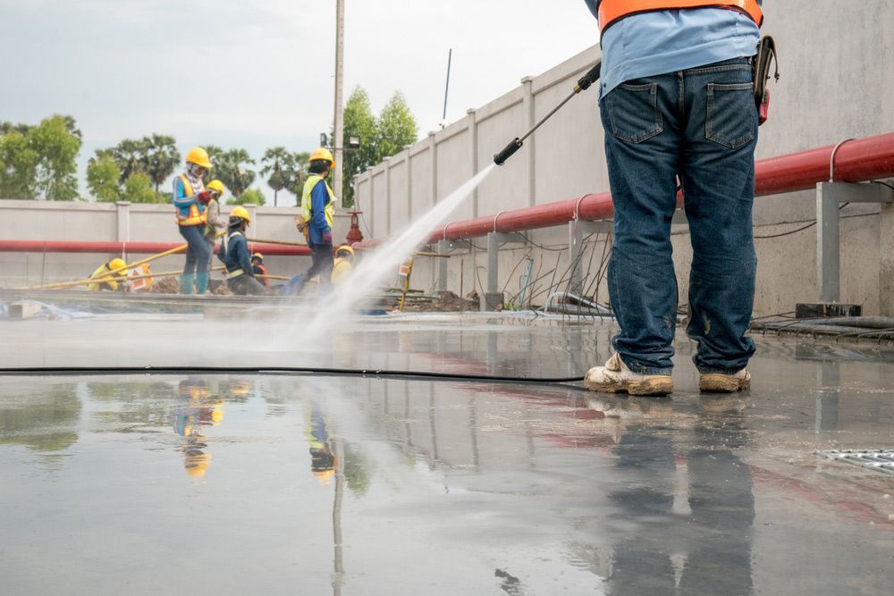 A Man Is Using a High Pressure Washer to Clean a Concrete Floor — Haydyn's Cleaning In Point Vernon, QLD