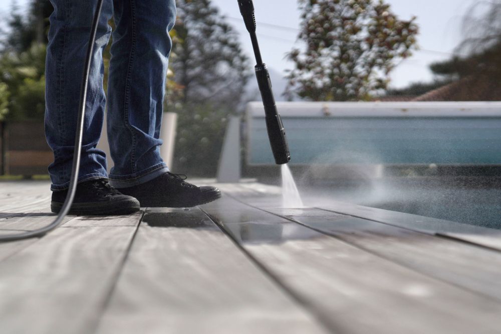 A Man Is Using a High Pressure Washer to Clean a Wooden Deck Next to A Pool — Haydyn's Cleaning In Dundowran, QLD
