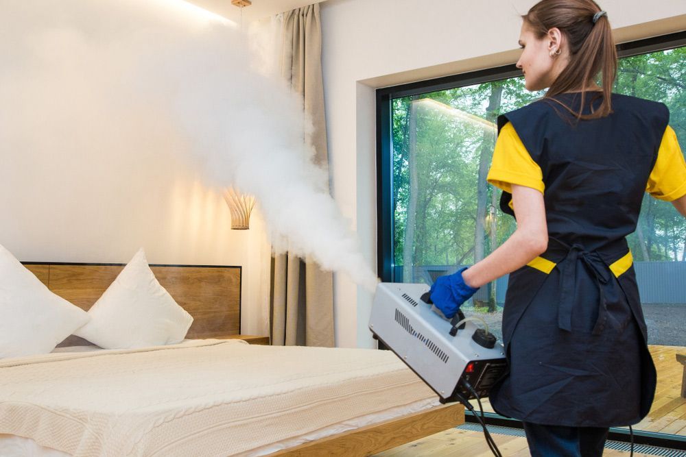 A Woman Is Disinfecting a Bedroom with A Machine — Haydyn's Cleaning In Urraween, QLD