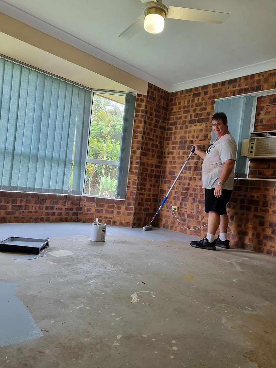 A Man Is Painting the Floor of A Room with A Roller — Haydyn's Cleaning In Urraween, QLD