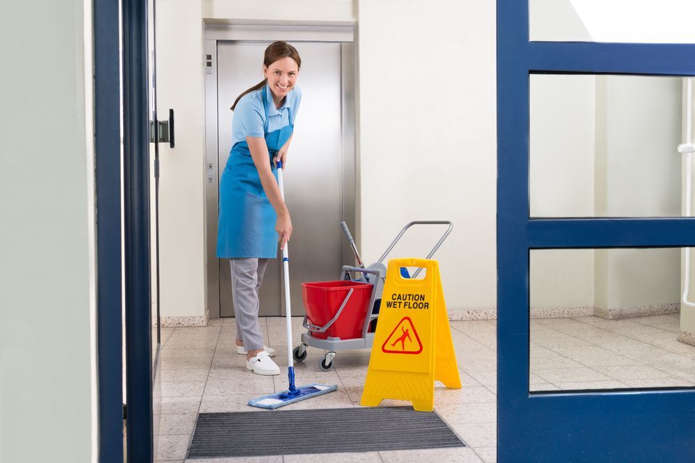 A Woman Is Mopping the Floor Next to A Caution Sign — Haydyn's Cleaning In Craignish, QLD