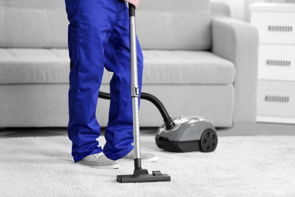 A Person Is Using a Vacuum Cleaner to Clean a Carpet in A Living Room — Haydyn's Cleaning In Dundowran, QLD