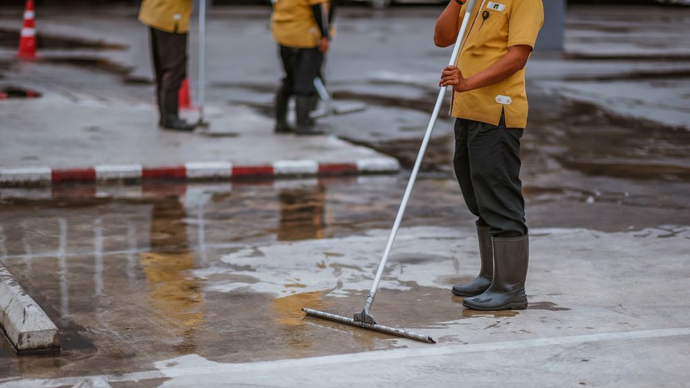 A Man Is Cleaning a Parking Lot with A Mop — Haydyn's Cleaning In Kawungan, QLD