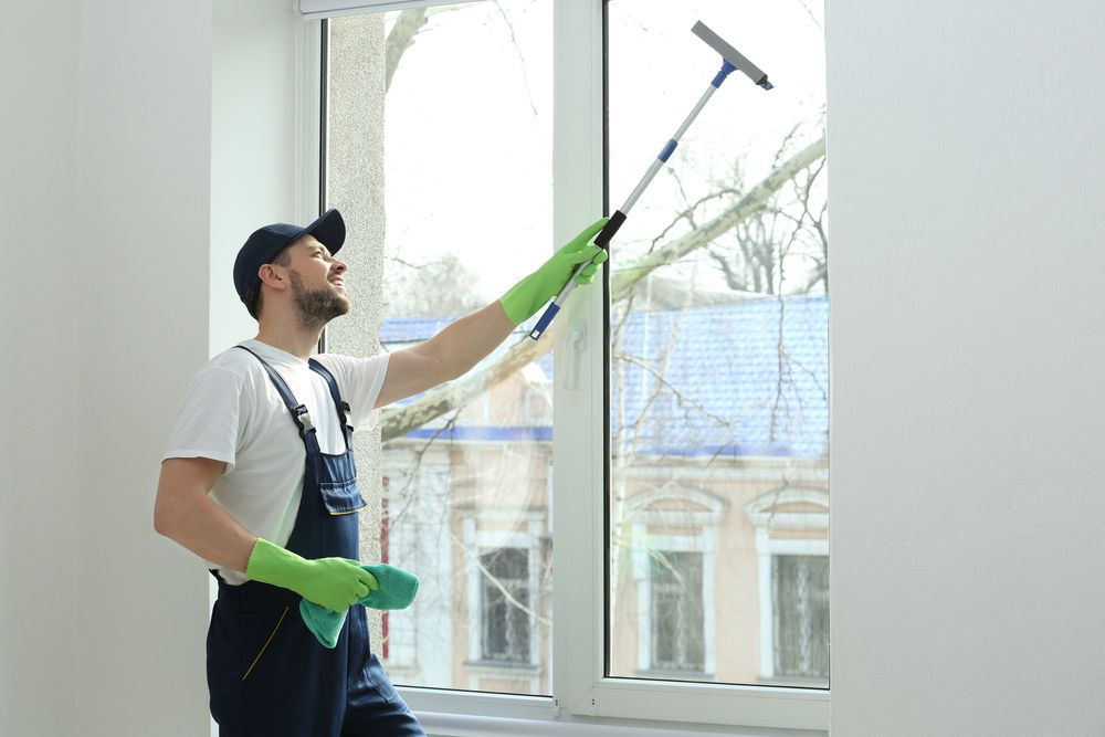 A Man Is Cleaning a Window with A Squeegee — Haydyn's Cleaning In Dundowran, QLD