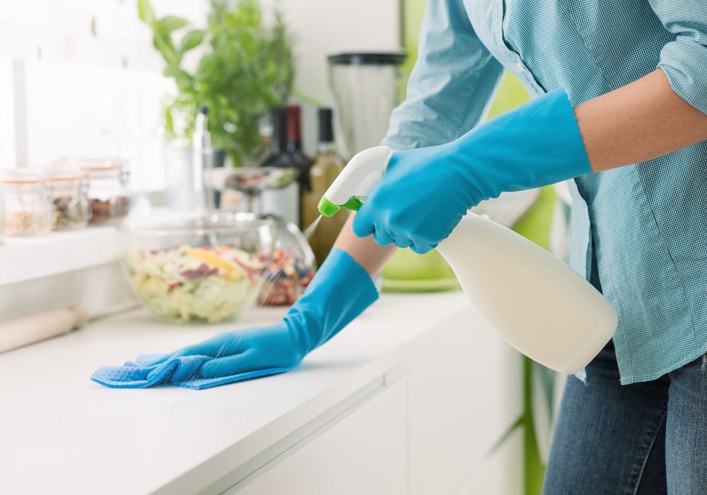 A Person Wearing Blue Gloves Is Cleaning a Kitchen Counter with A Spray Bottle — Haydyn's Cleaning In Urangan, QLD