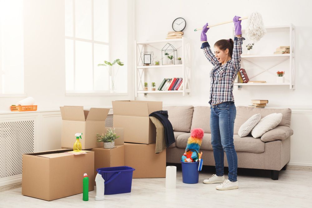 A Woman Is Cleaning a Living Room with Boxes and Cleaning Supplies — Haydyn's Cleaning In Urraween, QLD