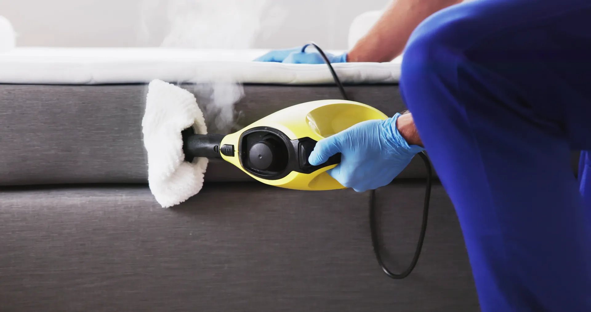 Person Using a Steam Cleaner to Clean a Gray Couch — Haydyn's Cleaning In Urraween, QLD