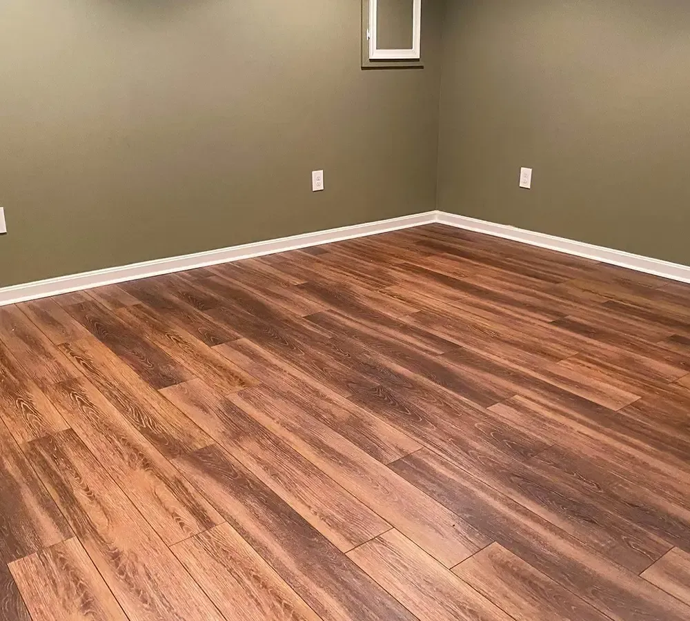 An empty room with muted olive-green walls, white trim, and light-brown wood-look plank flooring.
