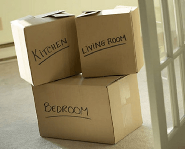 Three cardboard boxes labeled kitchen living room and bedroom are stacked on top of each other
