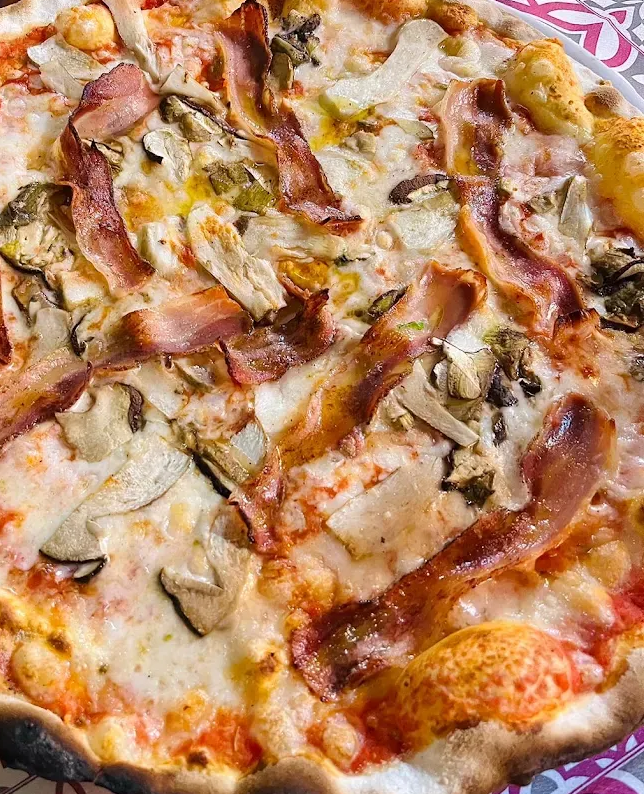 Pizza con formaggio fuso, funghi e prosciutto su un piatto decorato.