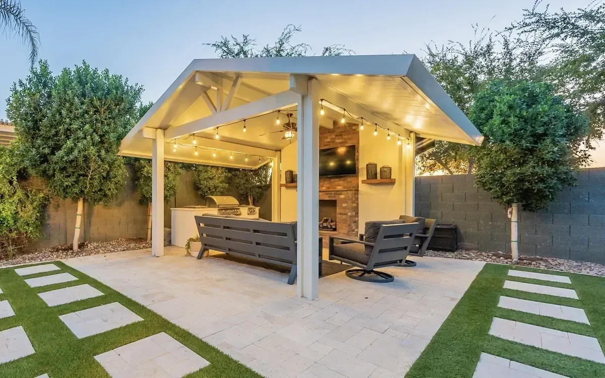 Backyard gazebo with white beams, stone posts, and picnic tables on a paved patio