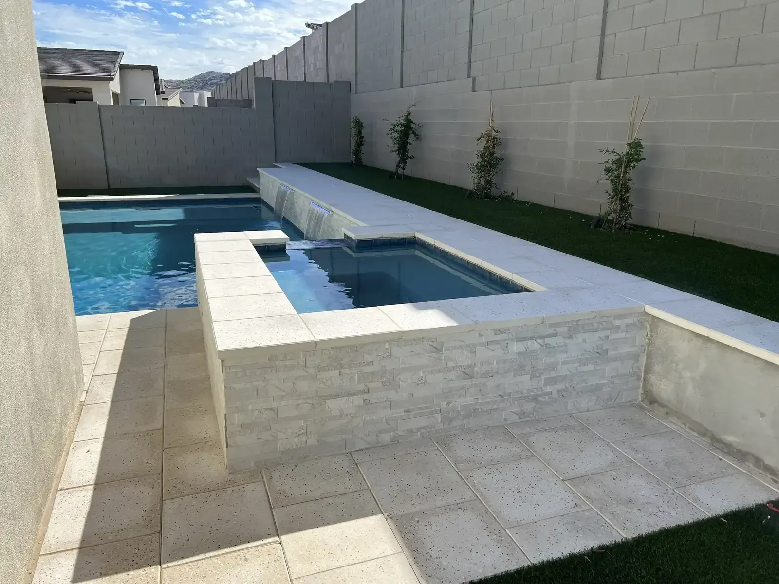 Modern backyard pool with raised spa, white stone decking, and gray privacy walls