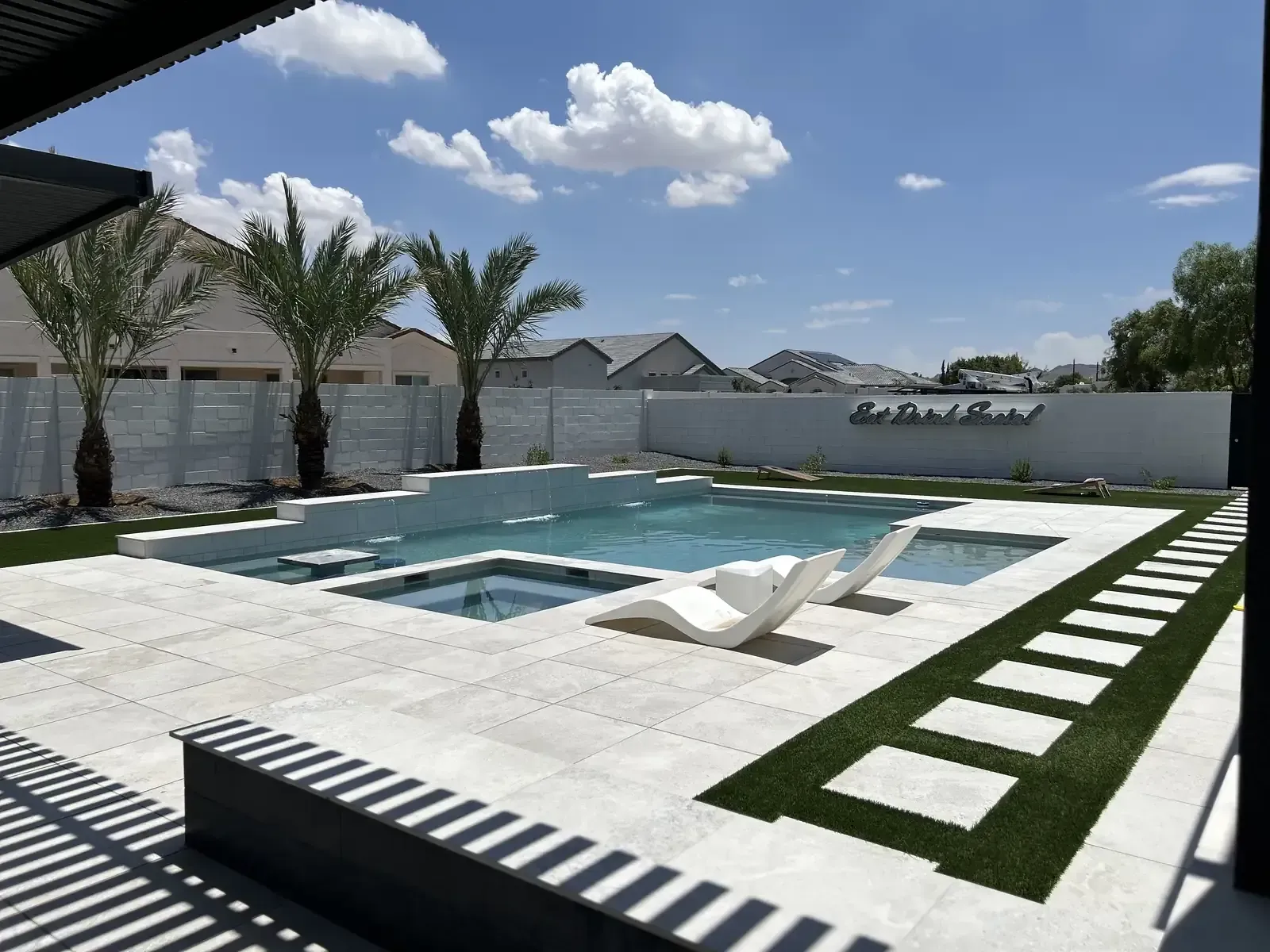 Backyard pool with stone wall, green lawn, and string lights under a blue sky