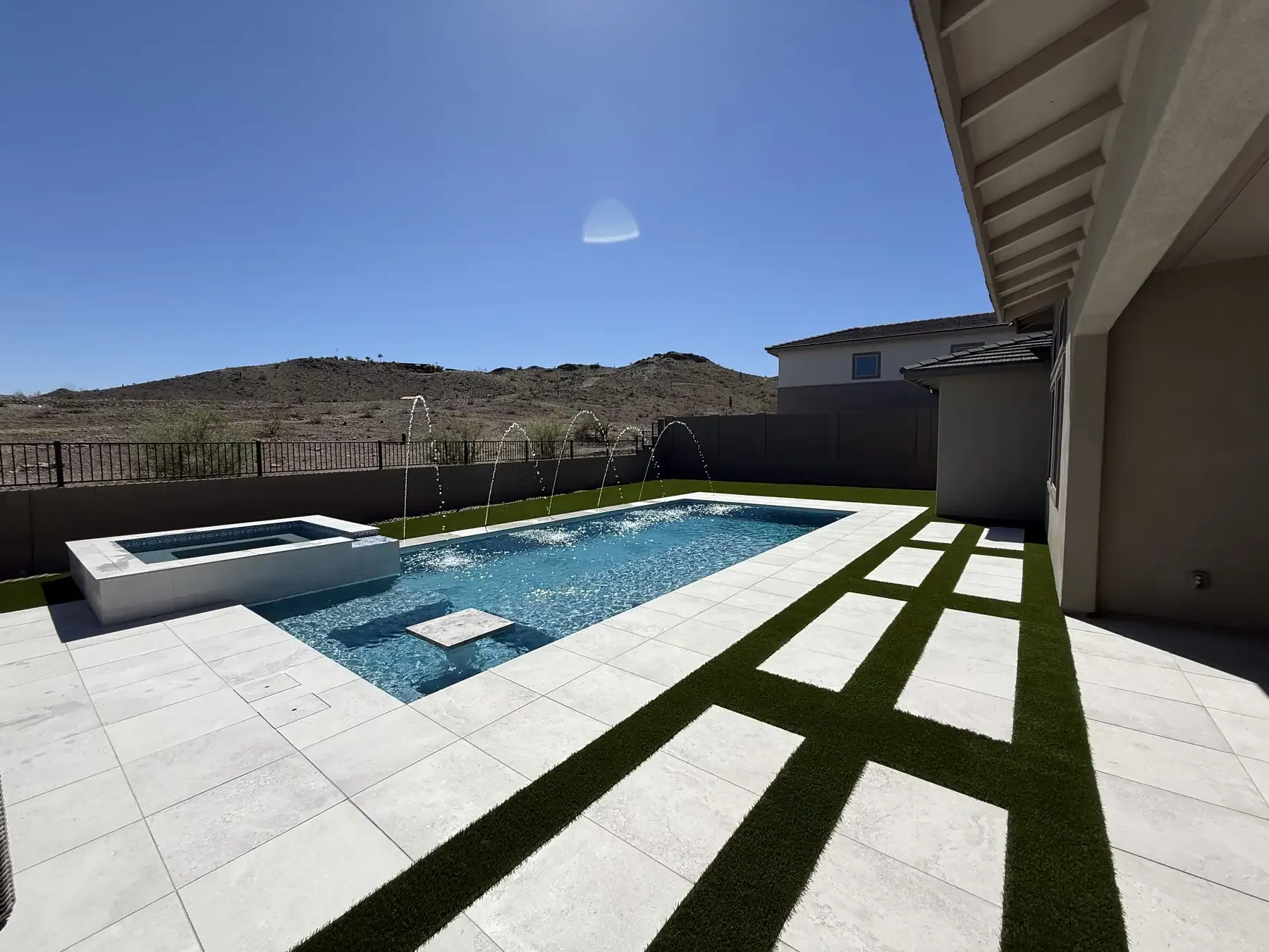 Backyard pool with stone wall, green lawn, and string lights under a blue sky