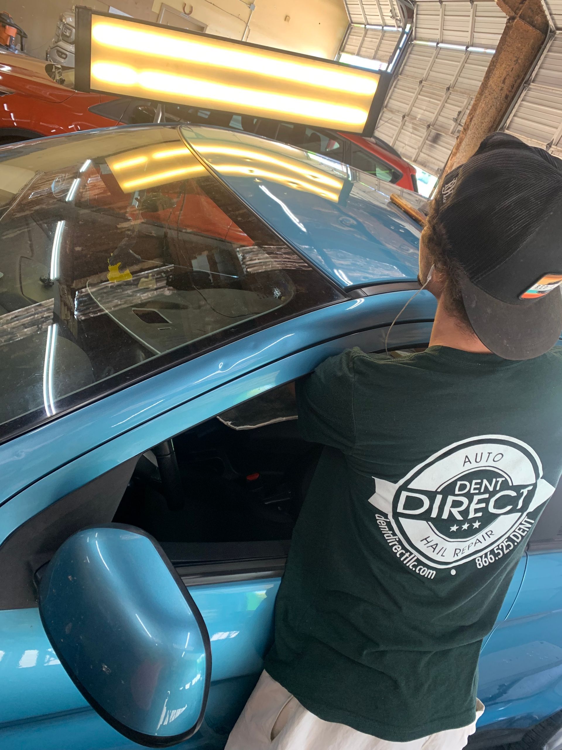 A man in a green shirt is standing next to a blue car.