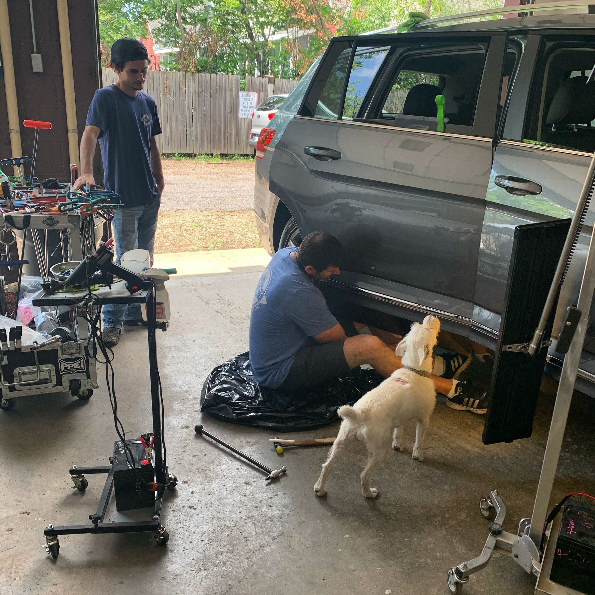 A man and a dog are working on a car in a garage